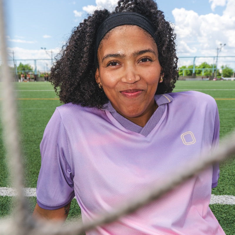 Woman wearing a pastel pink and purple sports jersey on a soccer field.
