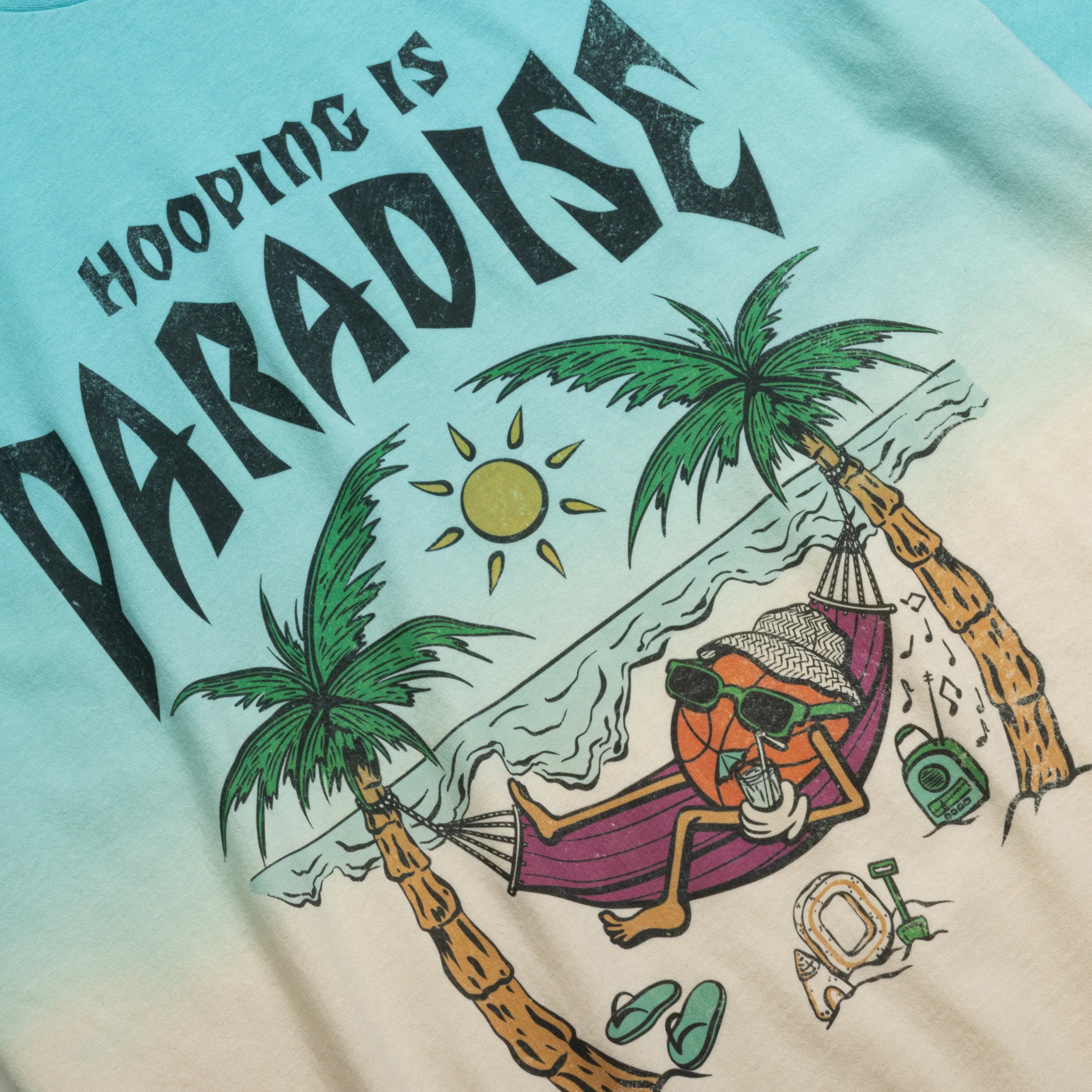 T-shirt with a tropical design featuring a basketball in a hammock on a beach with palm trees and the text 'Hooping is Paradise'.